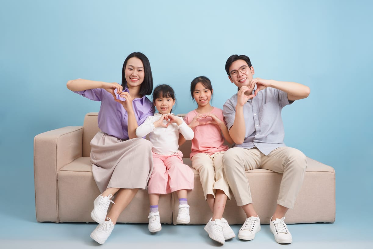 Smiling Asian family sitting together on a sofa at home, parents with two children sharing a happy moment.